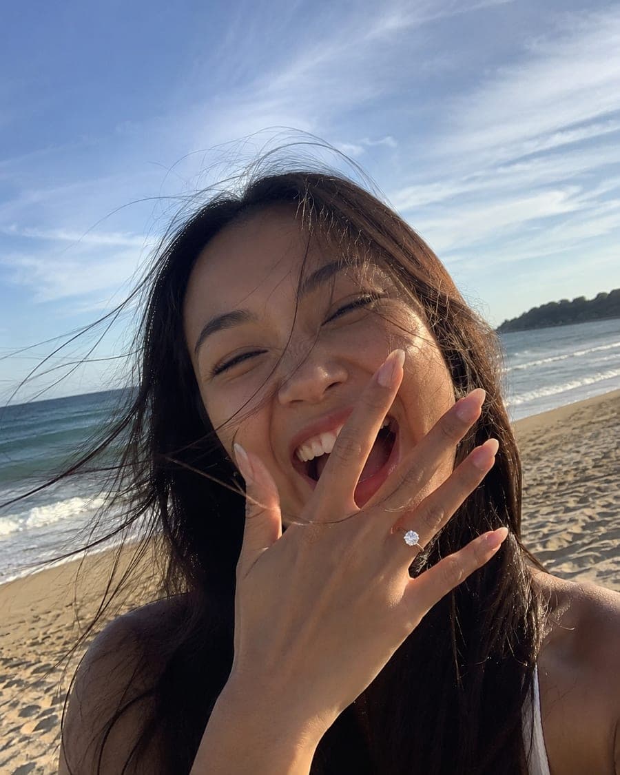 Mujer riendo en la playa mientras enseña su nuevo anillo de compromiso