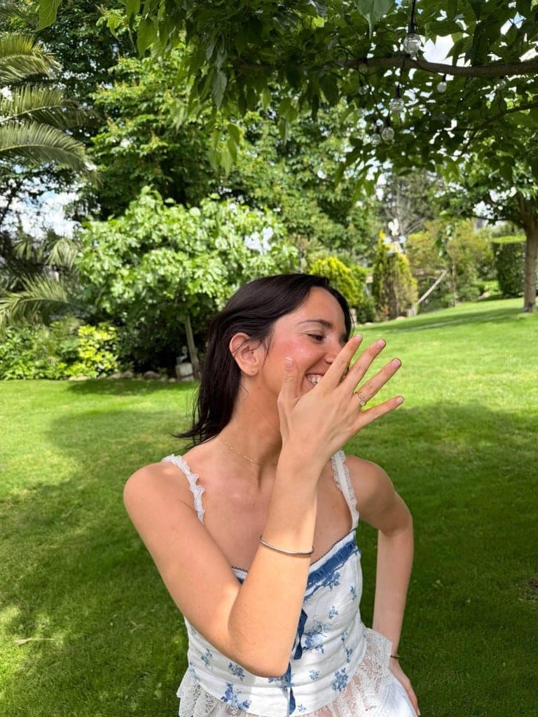 Mujer sonriendo mientras enseña su anillo de compromiso en un jardín